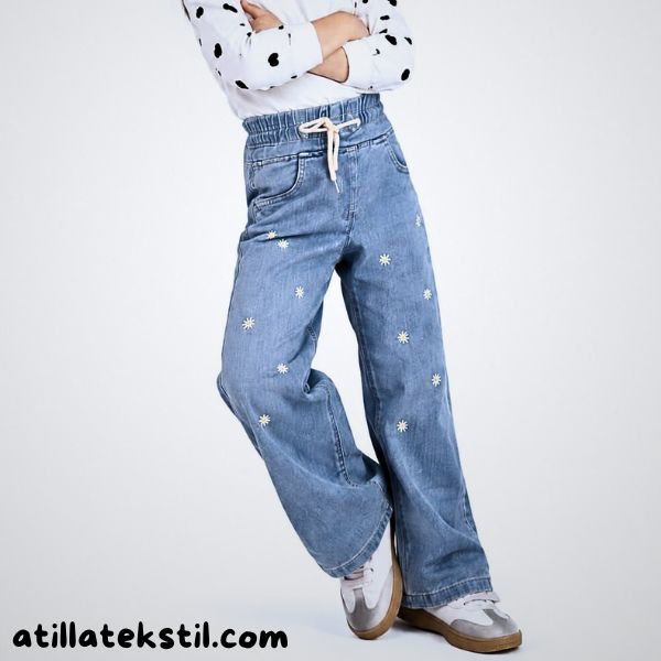 Lastikli kız çocuk kot pantolonu, beyaz denim kumaş üzerine bebek desenli beyaz çiçek detayları, rahat kesim çocuk kot pantolonu modeli